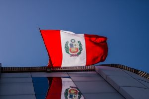National Peruvian flag waving prominently against a clear blue sky, reflecting on a building.