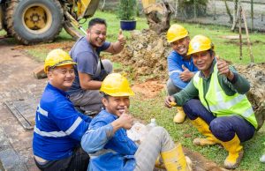 Group of smiling construction workers in safety gear taking a break outside.
