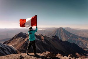 A climber waves the Peruvian flag on a mountain peak with a breathtaking view of the Andes.